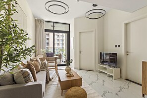 A modern living room with a sofa, coffee table, TV, and a large window with a view of buildings. - Silkhaus Canal Walk 1BR Stay in Al Maryah Island (Abu Dhabi)