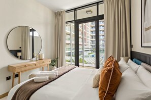 A hotel room with a bed, a round mirror, a wooden console table, a potted plant, and a view of the outside. - Silkhaus Canal Walk 1BR Stay in Al Maryah Island (Abu Dhabi)