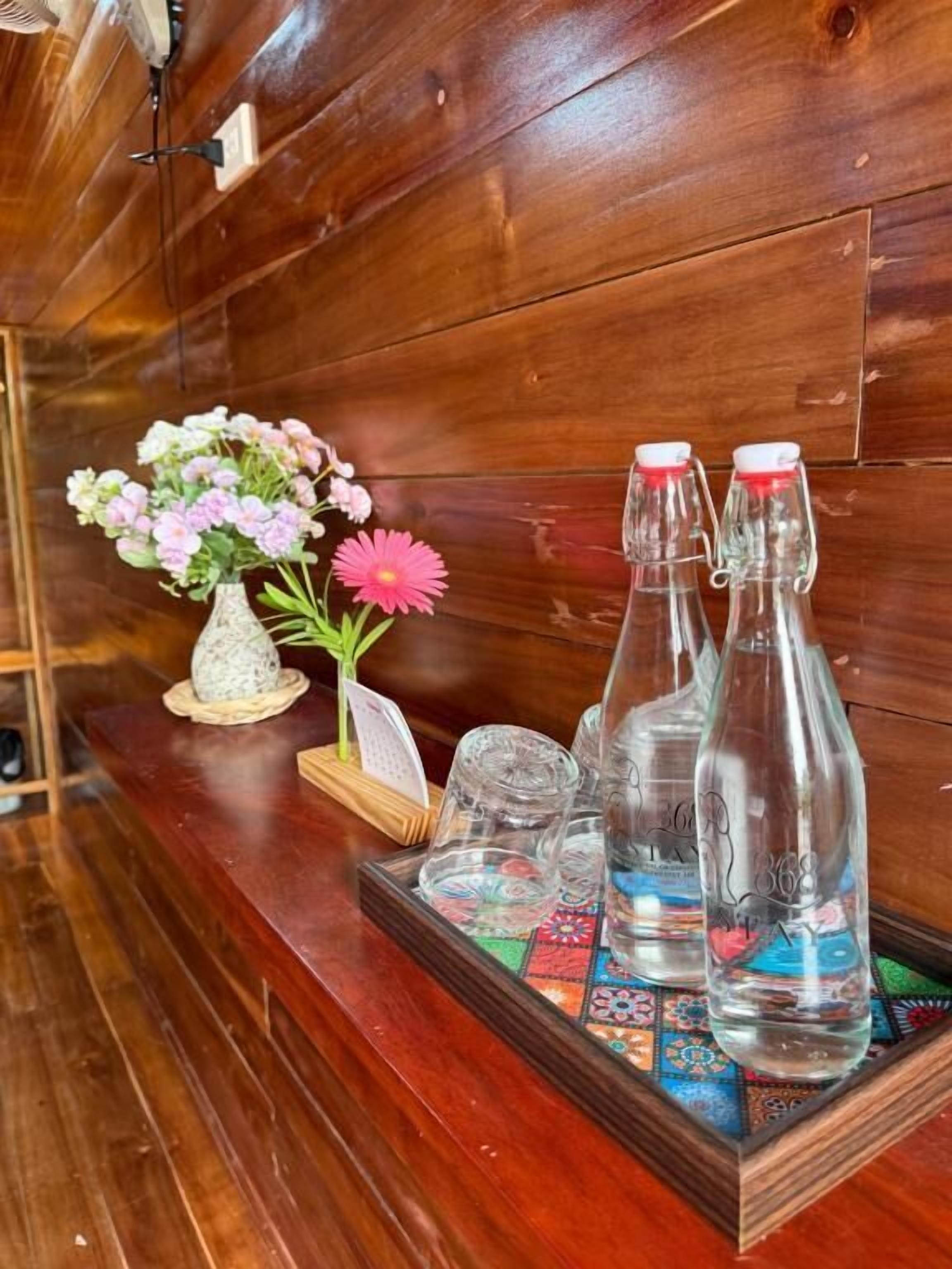 Un mur en bois sur lequel est fixée une étagère en bois, laquelle supporte un vase de fleurs, une bouteille en verre et un plateau contenant des bouteilles en verre et une assiette décorative.