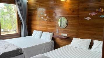 A room with two beds, wooden walls, a round mirror, and a window with curtains.