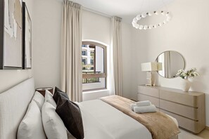 Ein Hotelzimmer mit einem Bett, einem Schminktisch, einem Spiegel, einem Fenster mit Vorhängen und Blick nach draußen.