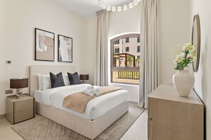 Ein Hotelzimmer mit Bett, Nachttischen, einem Schminktisch und einem Spiegel, mit Blick auf Gebäude.