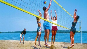 A group of people playing beach volleyball on a sandy beach with a clear blue sky and calm water in the background. - Gemutlich Eingerichteter Doppelbungalow mit Garten in Mirow (Mirow)