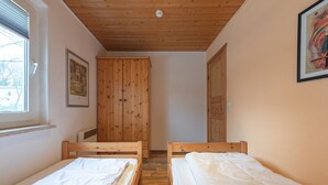 A room with two wooden beds, a wooden wardrobe, a framed picture on the wall, and a window. - Gemutlich Eingerichteter Doppelbungalow mit Garten in Mirow (Mirow)
