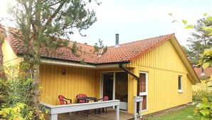 A yellow building with a red-tiled roof, a covered porch with chairs, and a small table. - Gemutlich Eingerichteter Doppelbungalow mit Garten in Mirow (Mirow)
