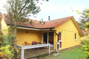 A yellow building with a red-tiled roof, a covered porch with chairs, and a small table. - Gemutlich Eingerichteter Doppelbungalow mit Garten in Mirow (Mirow)
