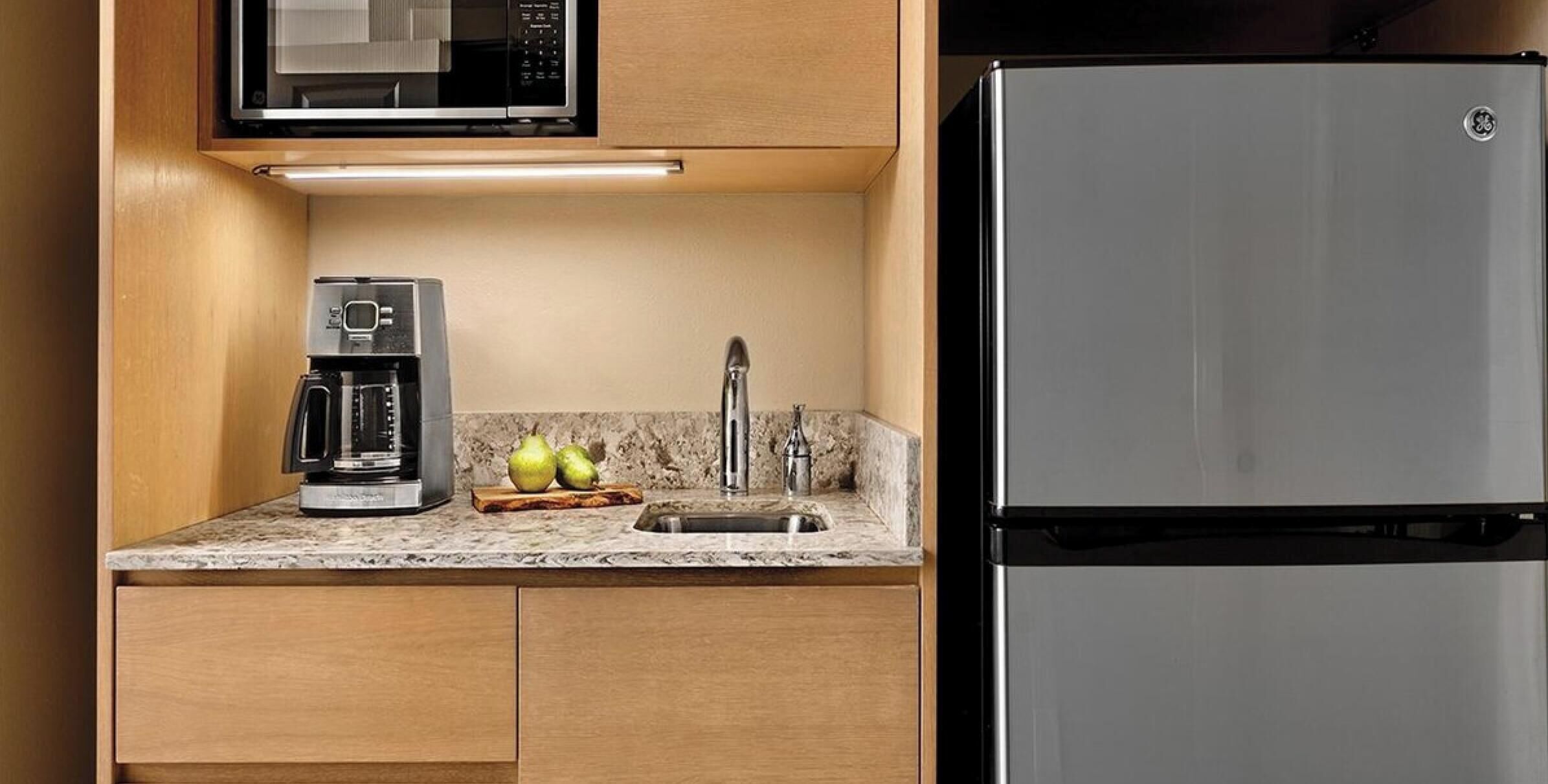A compact kitchen with a built-in microwave, a coffee maker, a sink, and a stainless steel refrigerator.