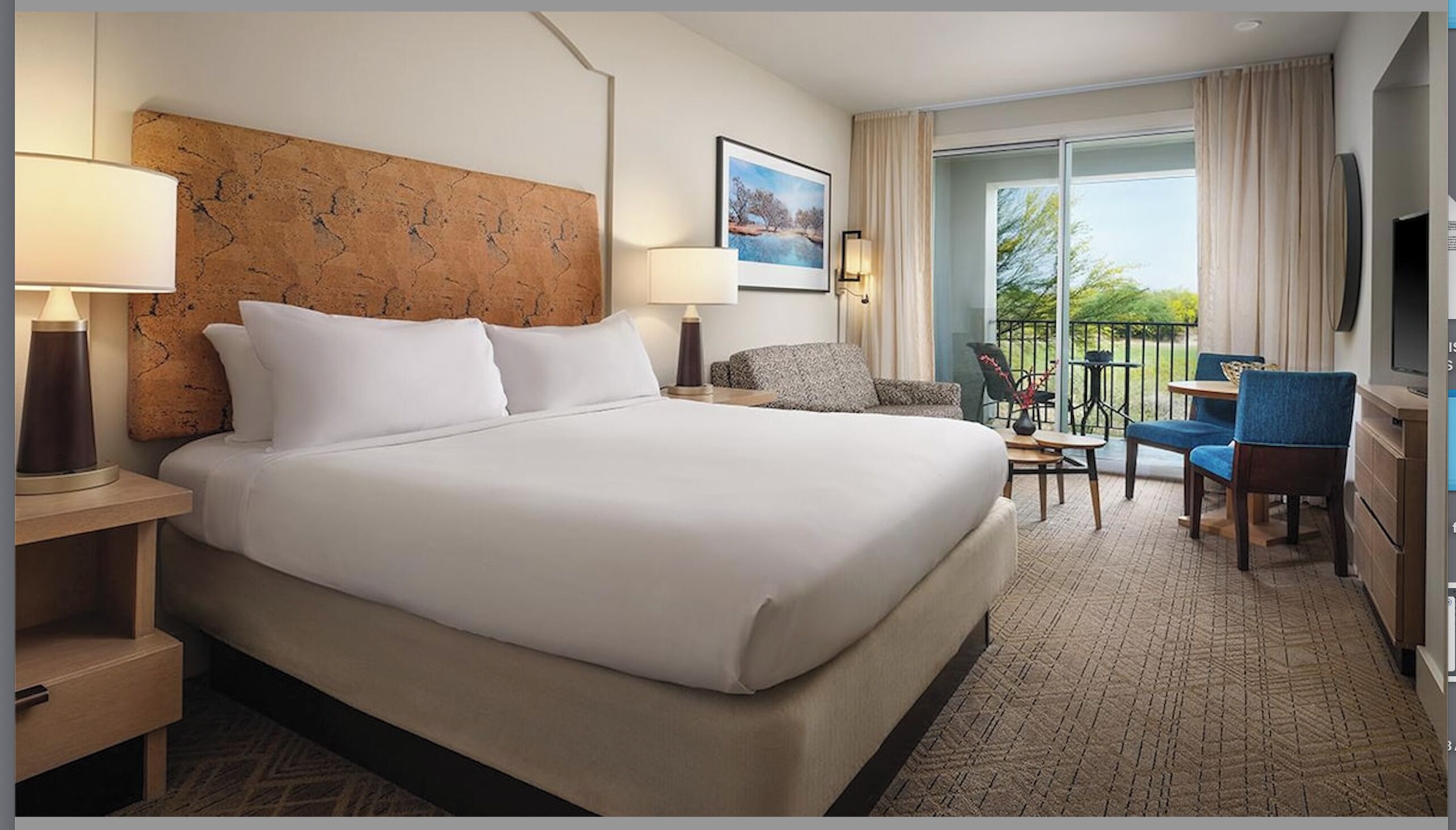 A hotel room with a large bed, a desk with a chair, a small table with a chair, and a balcony with a view.