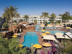 Ein Hotelpoolbereich mit mehreren Pools, Liegestühlen, Sonnenschirmen und Palmen.