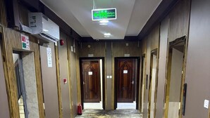 Un pasillo de hotel con puertas a ambos lados, alfombra estampada y un equipo de aire acondicionado en la pared.