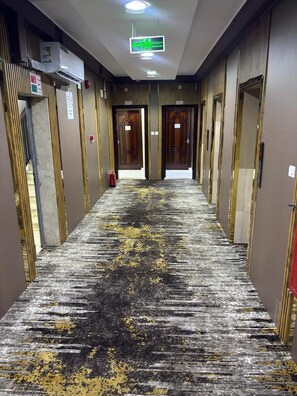 A hotel corridor with doors on both sides, a patterned carpet, and an air conditioning unit on the wall. - Sedan Hotel (Makkah)