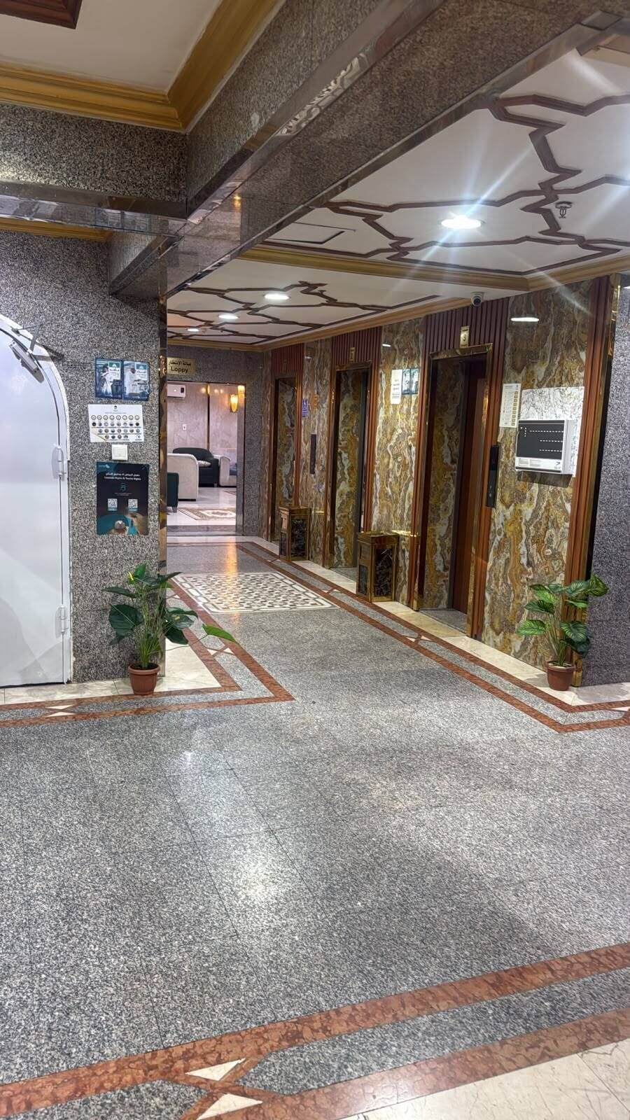 A hotel lobby with a marble floor, a reception desk, and a staircase leading to the upper floors.