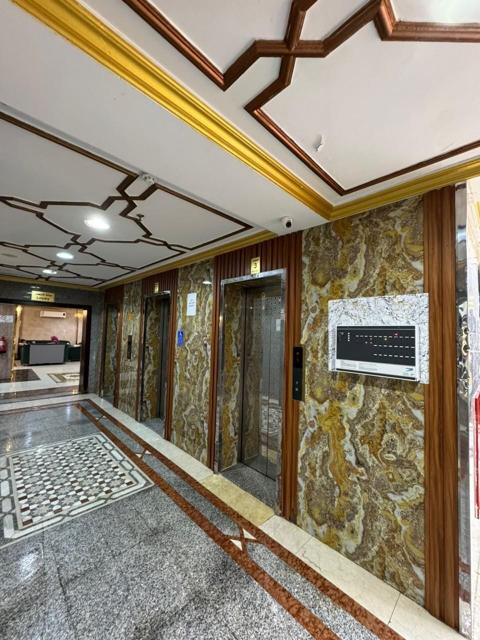 A hotel lobby with marble flooring, a reception desk, and elevators.