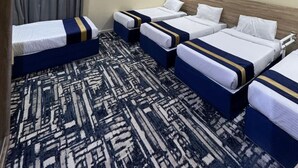 Habitación de hotel con cuatro camas individuales en fila, alfombra estampada y cabecera de madera.