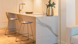 A modern kitchen with a marble countertop, two bar stools, a pendant light, and a floor lamp. - Pearl: Luxury and Design in the Heart of Viale Ceccarini (Riccione)