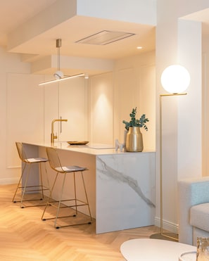 Eine moderne Küche mit Marmorarbeitsplatte, zwei Barhocker, einer Pendelleuchte und einer Stehlampe.