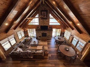 Amplia habitación estilo loft con chimenea de piedra, vigas de madera, ventanas grandes y un rincón de descanso acogedor.