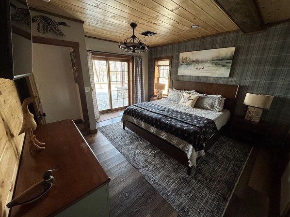 A bedroom with a bed, a wooden dresser, a chandelier, and a painting on the wall.