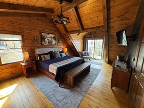 A wooden cabin bedroom with a bed, bench, nightstands, and a TV. - Luxury 7BR Lakefront Log Lodge; Sleeps 18 (DuBois)
