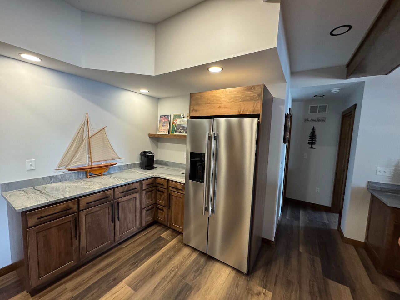 A kitchen with wooden cabinets, a stainless steel refrigerator, and a marble countertop.