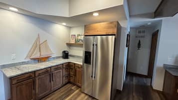 A kitchen with wooden cabinets, a stainless steel refrigerator, and a marble countertop.