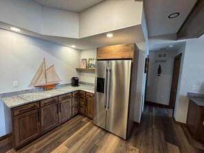 Cocina con gabinetes de madera, refrigerador de acero inoxidable y encimera de mármol.