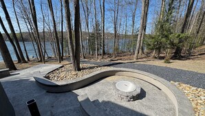 A concrete outdoor area with a circular seating arrangement, surrounded by trees and a body of water in the background. - Luxury 7BR Lakefront Log Lodge; Sleeps 18 (DuBois)