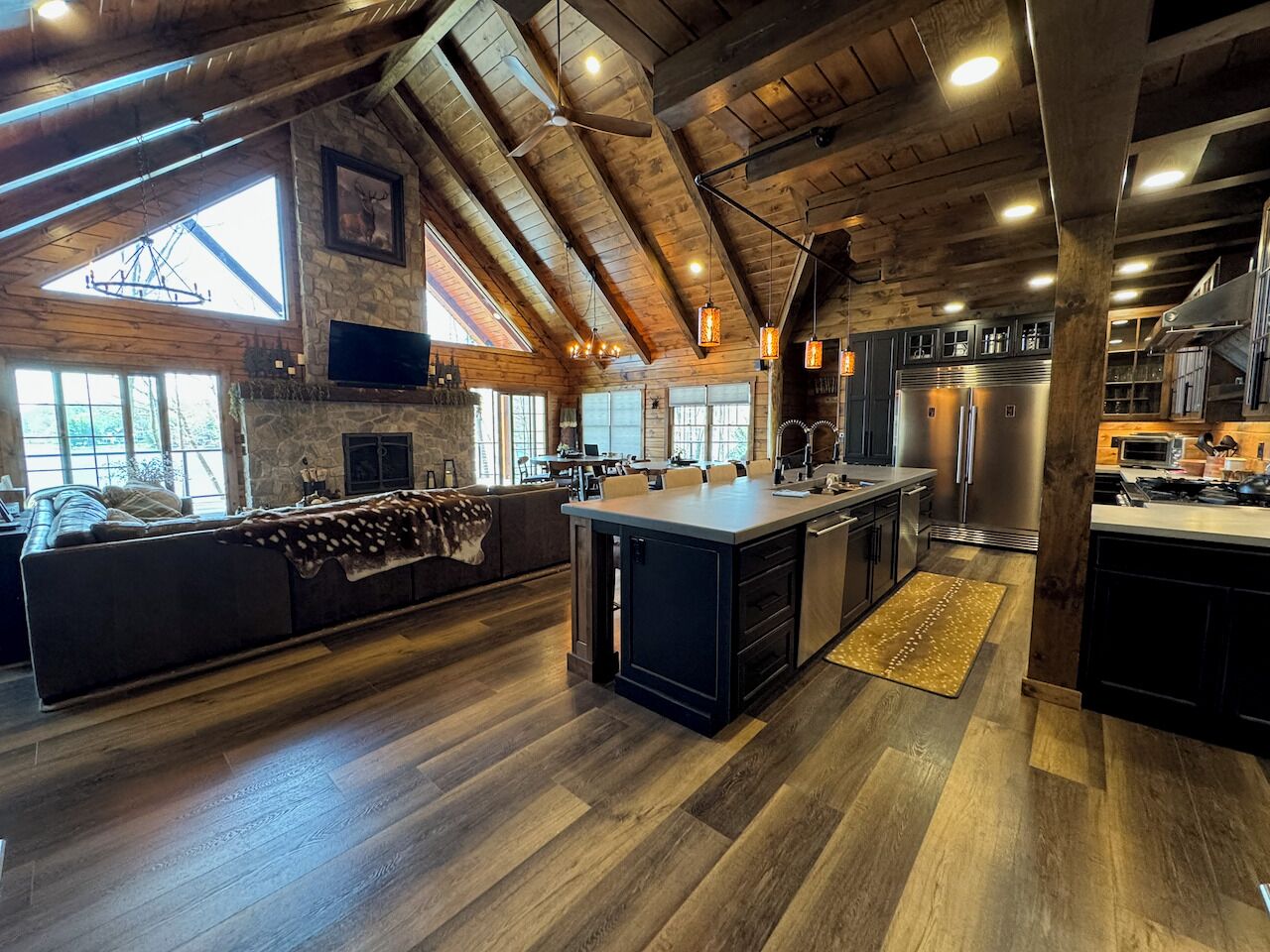 A spacious kitchen with a large island, wooden beams, and a stone wall.
