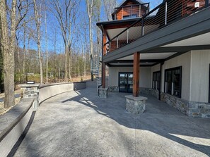 A modern building with a curved driveway, stone pillars, and a balcony overlooking a forested area.