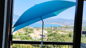 A view through a window with a blue awning, overlooking a coastal area with buildings and greenery. - DUPLEX APART SLEEPS 5, AIR CONDITIONING, BEAUTIFUL SEA VIEW, POOL, 3 min BEACH (Grosseto-Prugna, PORTICCIO)