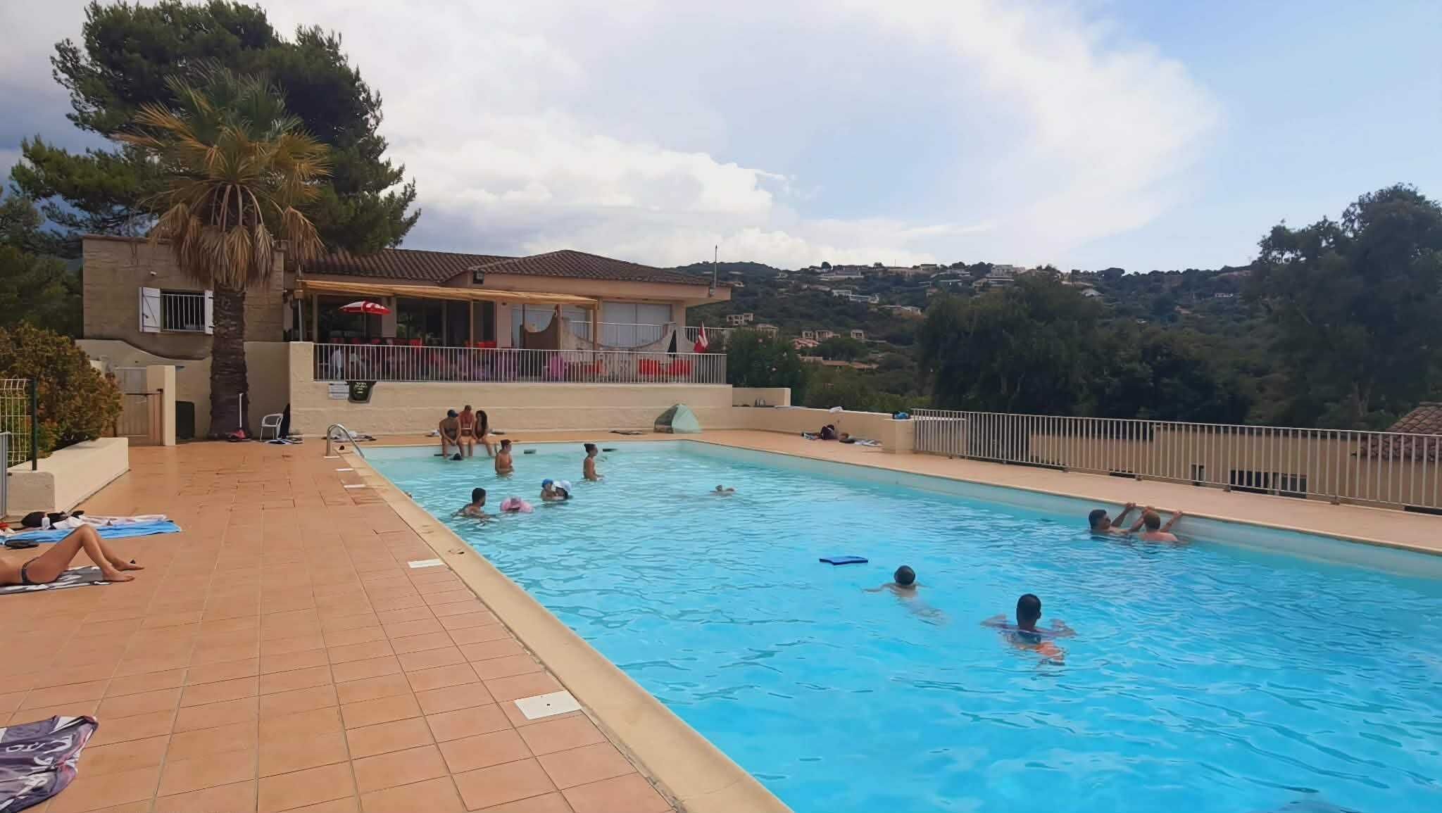 Una piscina con gente, un edificio con balcón y vistas del paisaje circundante.