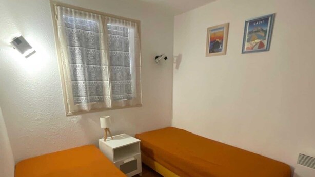A room with two beds, a small white bedside table, a window with patterned curtains, and two wall-mounted pictures. - DUPLEX APART SLEEPS 5, AIR CONDITIONING, BEAUTIFUL SEA VIEW, POOL, 3 min BEACH (Grosseto-Prugna, PORTICCIO)