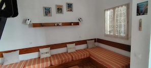 A room with a wooden bench bed, pillows with 'HOME' and 'AMORE' text, a shelf with a globe, and three framed pictures on the wall.