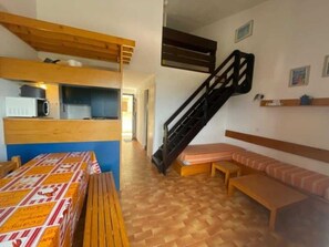 A room with a bunk bed, a staircase, a bench, and a table with a patterned tablecloth.