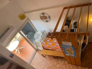 A room with a bed, a table, a chair, a radiator, a clock, and a window.
