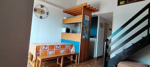 A room with a wooden table covered with a patterned tablecloth, a microwave, and a wooden staircase.