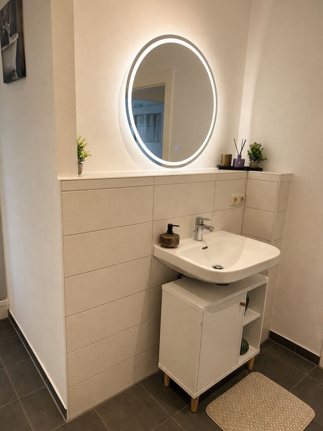 Ein modernes Badezimmer mit einem runden Spiegel, einem weißen Waschbecken und einer kleinen Ablage.