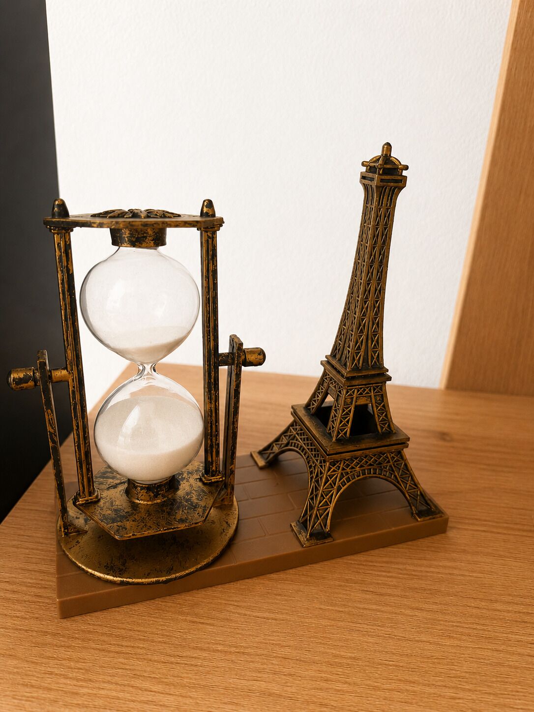 A brass hourglass and a miniature Eiffel Tower on a wooden base.