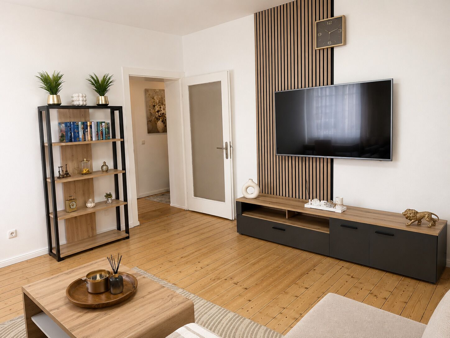 Ein modernes Wohnzimmer mit flachbildfernseher an einer Holzwand, einer Bücherwand und einem Couchtisch mit Tablett.