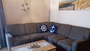 Ein Wohnzimmer mit einer Couch, einem Couchtisch mit Zeitungen und Kissen im maritimen Stil.
