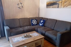 A living room with a sofa, a coffee table with newspapers, and nautical-themed pillows. - Modern Eingerichteter Doppelbungalow mit Garten im Ferienpark Mirow (Mirow)