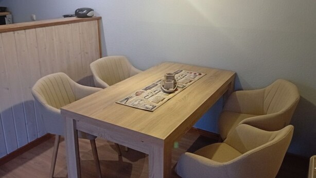 Ein Essbereich mit einem Holztisch, vier Stühlen, einer Lampe und einer kleinen Küchenzeile im Hintergrund.