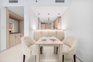 Un comedor moderno con una mesa de madera, dos sillas tapizadas y una cocina al fondo.
