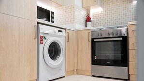 A compact kitchen with a washing machine, oven, and wooden cabinets. - StayShort - Prime 1 Bedroom Sleeps 2 in Palm Jumeirah (Dubai)