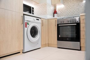 Cocina compacta con lavadora, horno y armarios de madera.