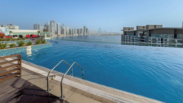 A rooftop pool with a city skyline view, a clear sky, and a calm water surface. - StayShort - Prime 1 Bedroom Sleeps 2 in Palm Jumeirah (Dubai)