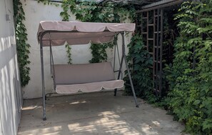 A metal swing chair with a canopy, positioned against a wall with climbing plants.