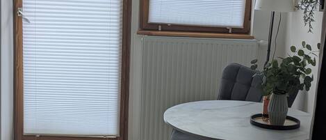 Une pièce dotée d’une porte-fenêtre coulissante, d’une table ronde avec une chaise, d’une plante en pot et d’un téléviseur fixé au mur.