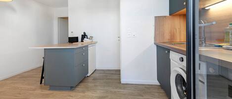 Une cuisine compacte dotée d’un lave-linge encastré, d’un petit îlot central avec un évier et d’un plan de travail en bois.