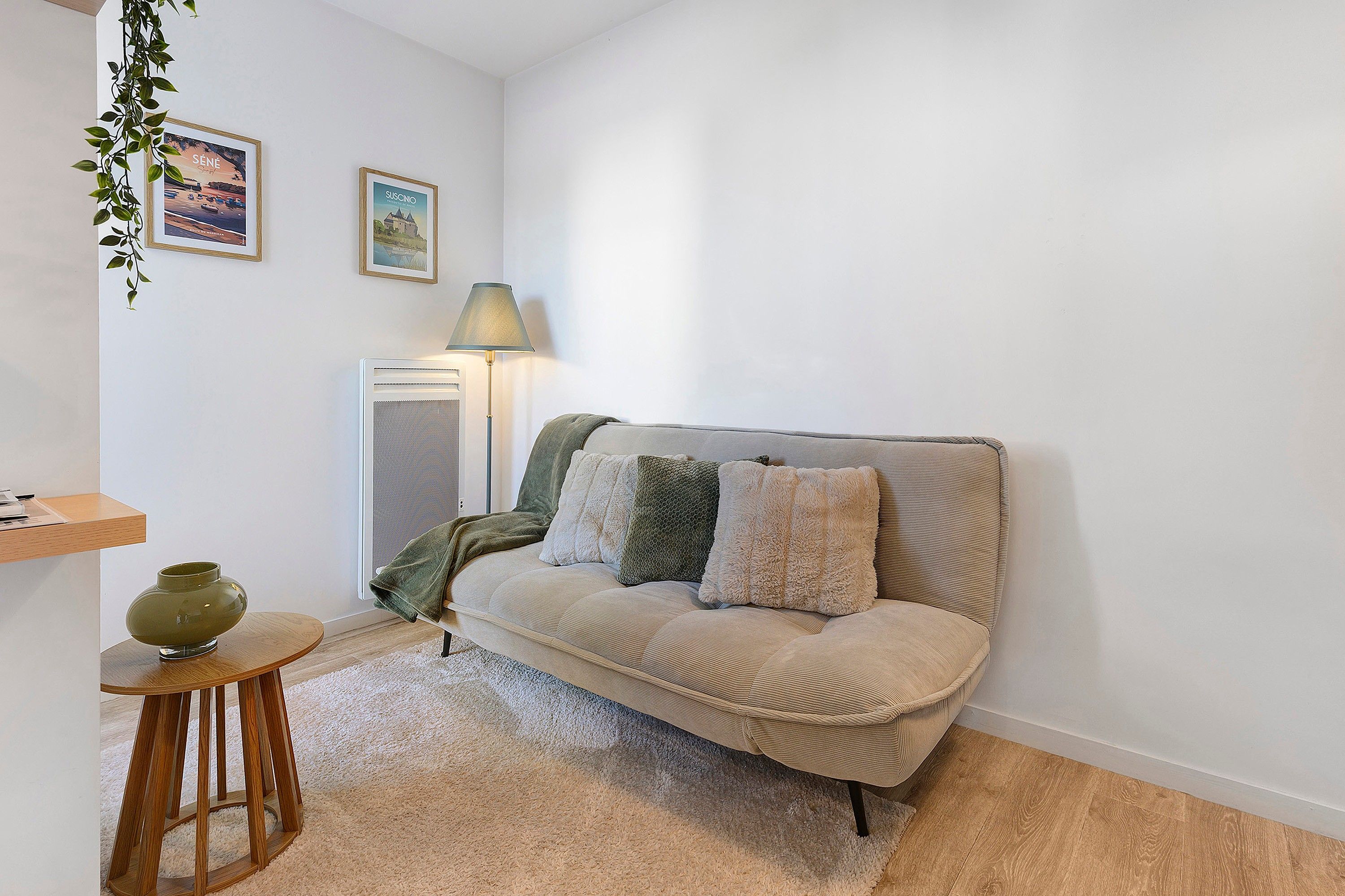 A cozy living room with a sofa, a lamp, a small table, and a decorative plant.